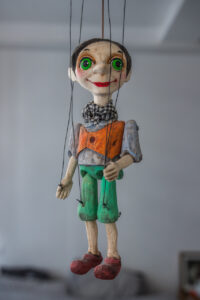 Eine Fadenpuppe (Marionette) aus Prag (Tschechische Republik). Ein schönes Nahaufnahme-Foto dieser seltsam aussehenden, kleinen Figur. Sie hängt in der Luft, trägt einen Schal, hat kurze Haare und große grüne Augen.