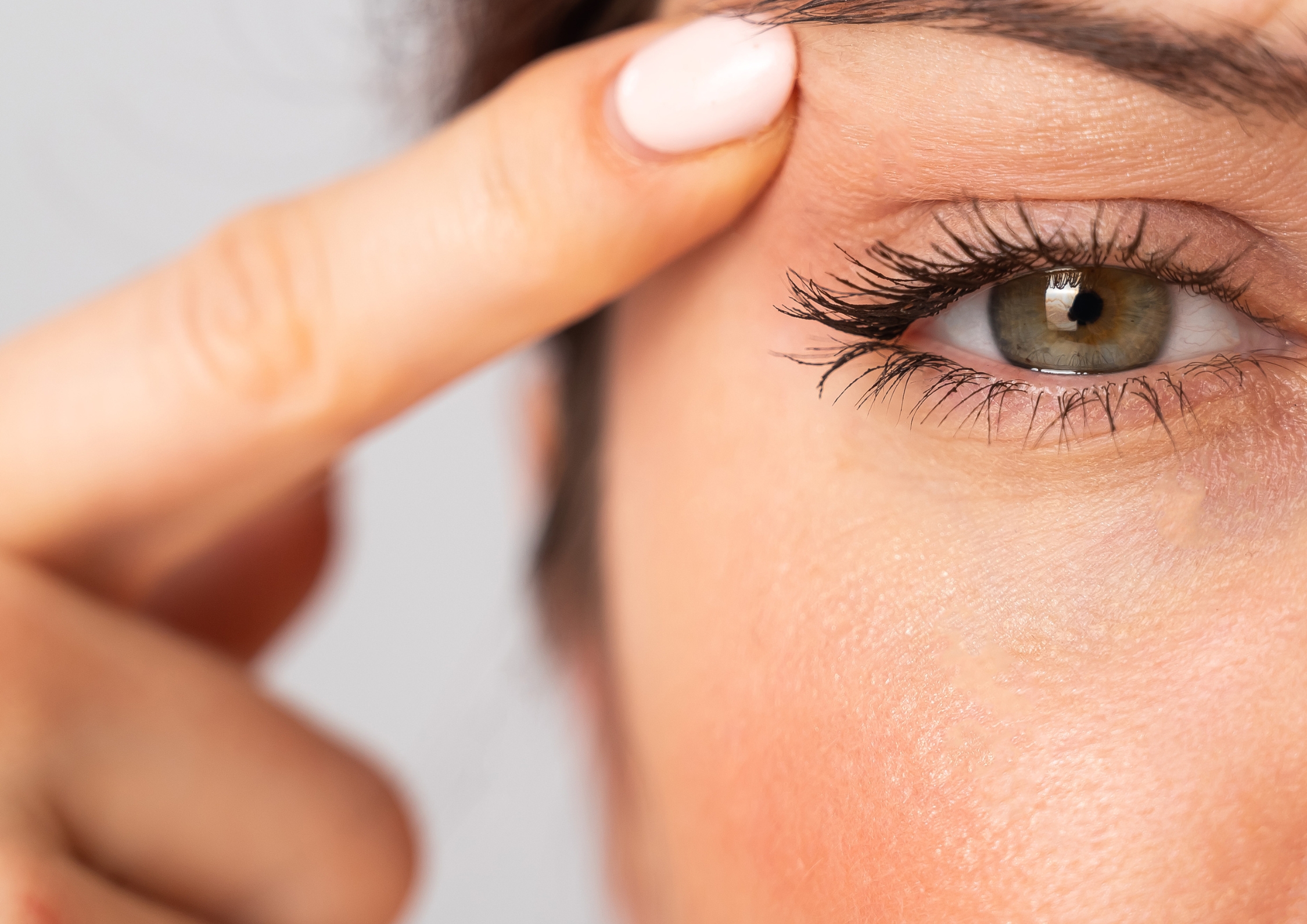 Eine Frau die mit einem Finger die überschüssige Haut am Auge etwas hochzieht.